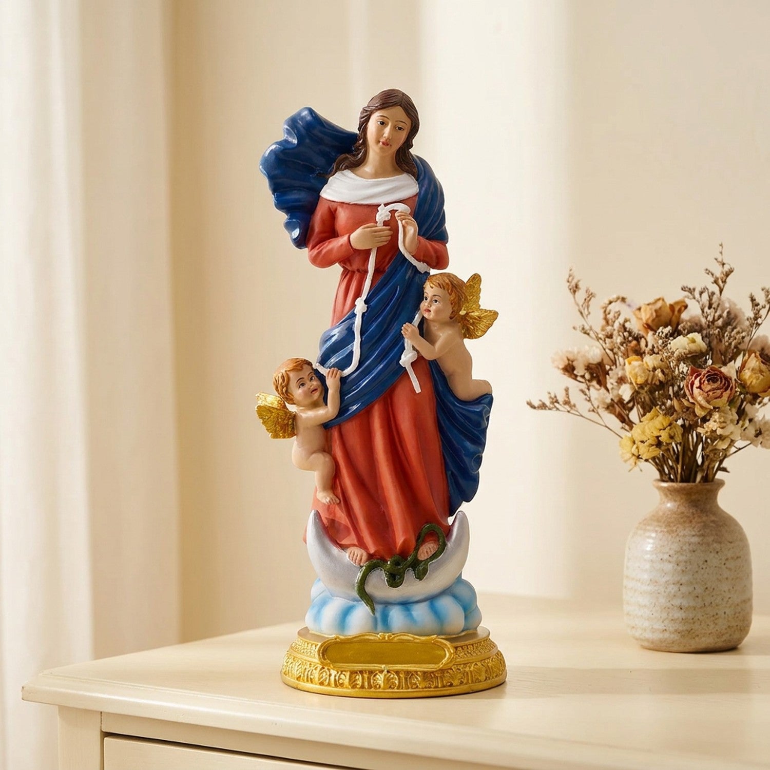 Figurine de la vierge Marie à la robe rouge sur une commode avec des fleurs séchées