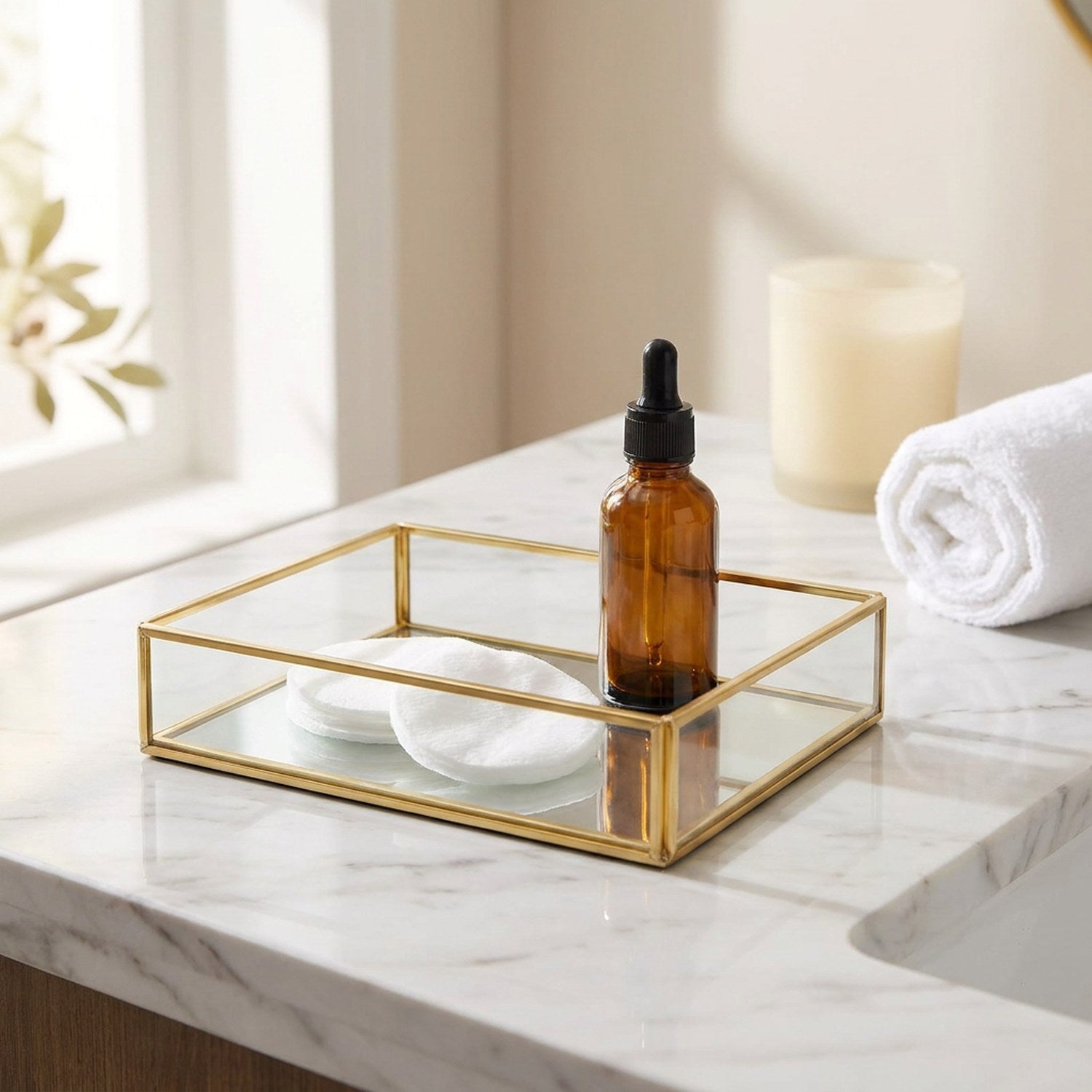 Plateau en verre et métal doré sur un plan de salle de bain avec cotons et flacon ambré