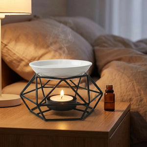 Brûle-parfum géométrique noir posé sur une table de chevet avec un flacon d'huile essentielle