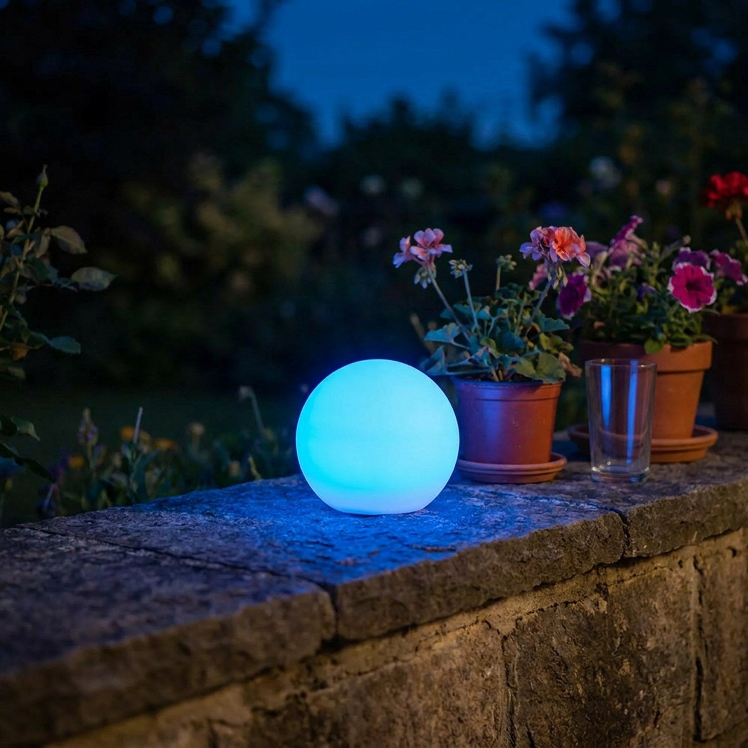 Boule lumineuse LED allumée en bleu sur un muret de jardin la nuit