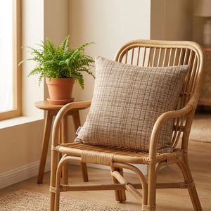 Housse de coussin beige sur un fauteuil en rotin près d'une fenêtre avec une plante verte