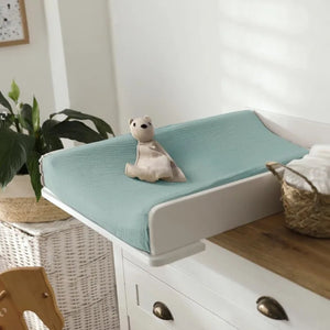 Housse de matelas à langer vert sauge sur un plan à langer avec doudou
