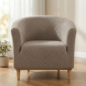 Fauteuil club recouvert de sa housse taupe près d une fenêtre voilée