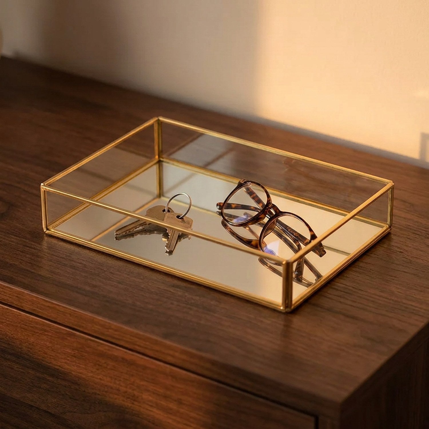 Plateau en verre et métal doré sur une console en bois avec des clés et des lunettes au coucher du soleil