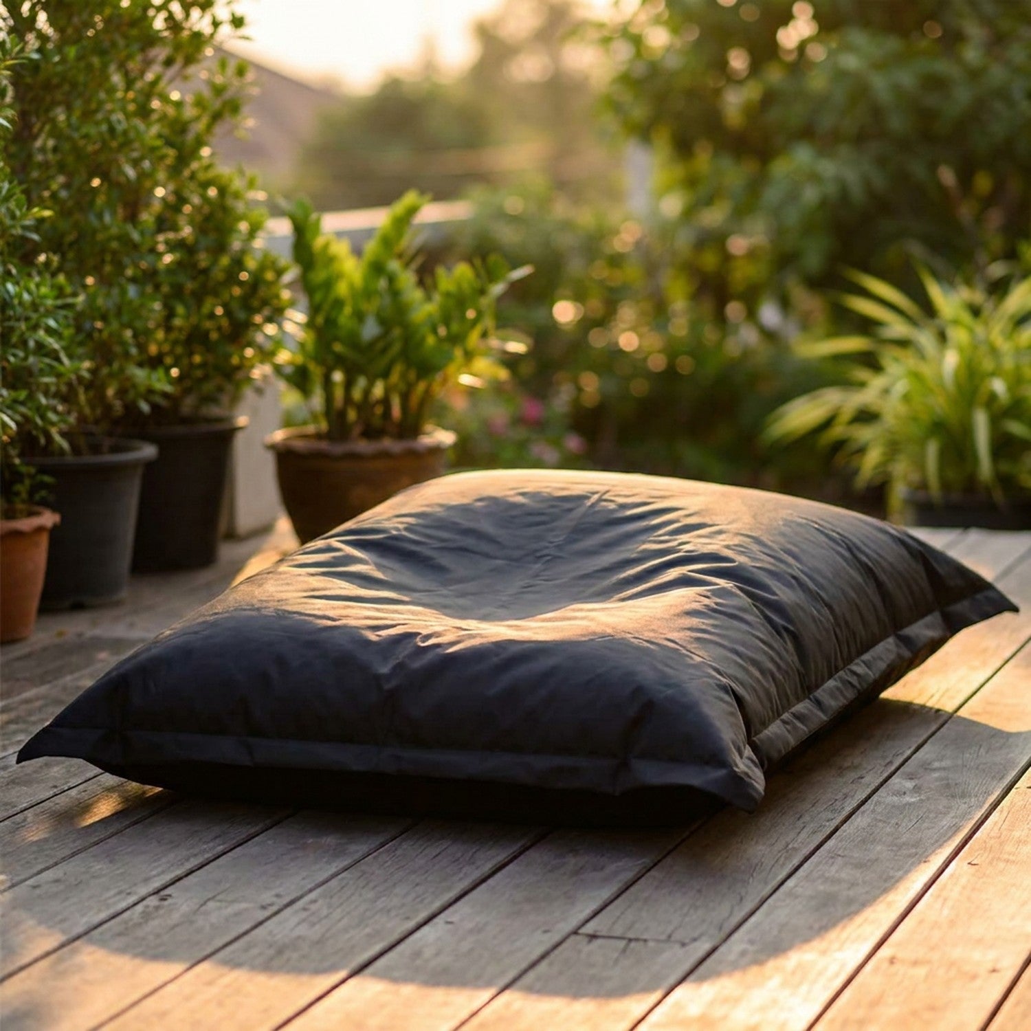 Housse de pouf géant noire imperméable installée sur une terrasse en bois au coucher du soleil