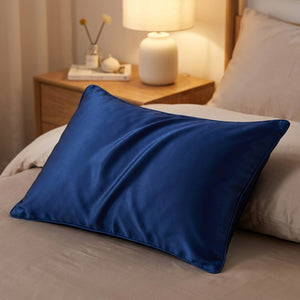 Taie d'oreiller en soie bleu foncé sur un lit avec lampe de chevet allumée le soir