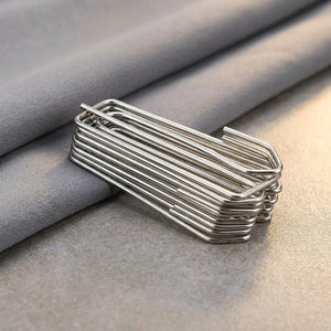 Pile de crochets à plis pour rideaux en acier inoxydable sur un tissu gris