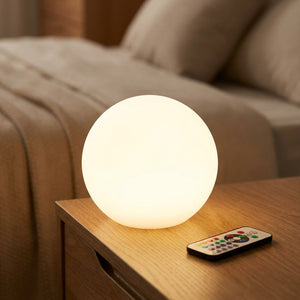 Boule lumineuse LED blanc chaud sur une table de chevet avec sa télécommande