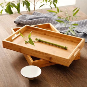 Deux plateaux en bambou empilés sur une table en bois avec un linge rayé