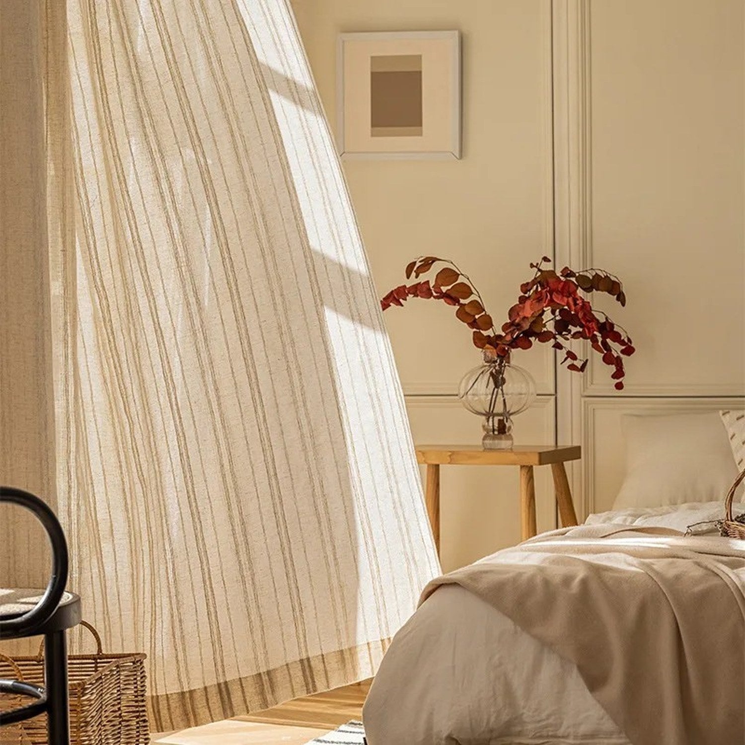 Rideau en gaze rayé beige suspendu devant une fenêtre baignée de lumière dans une chambre