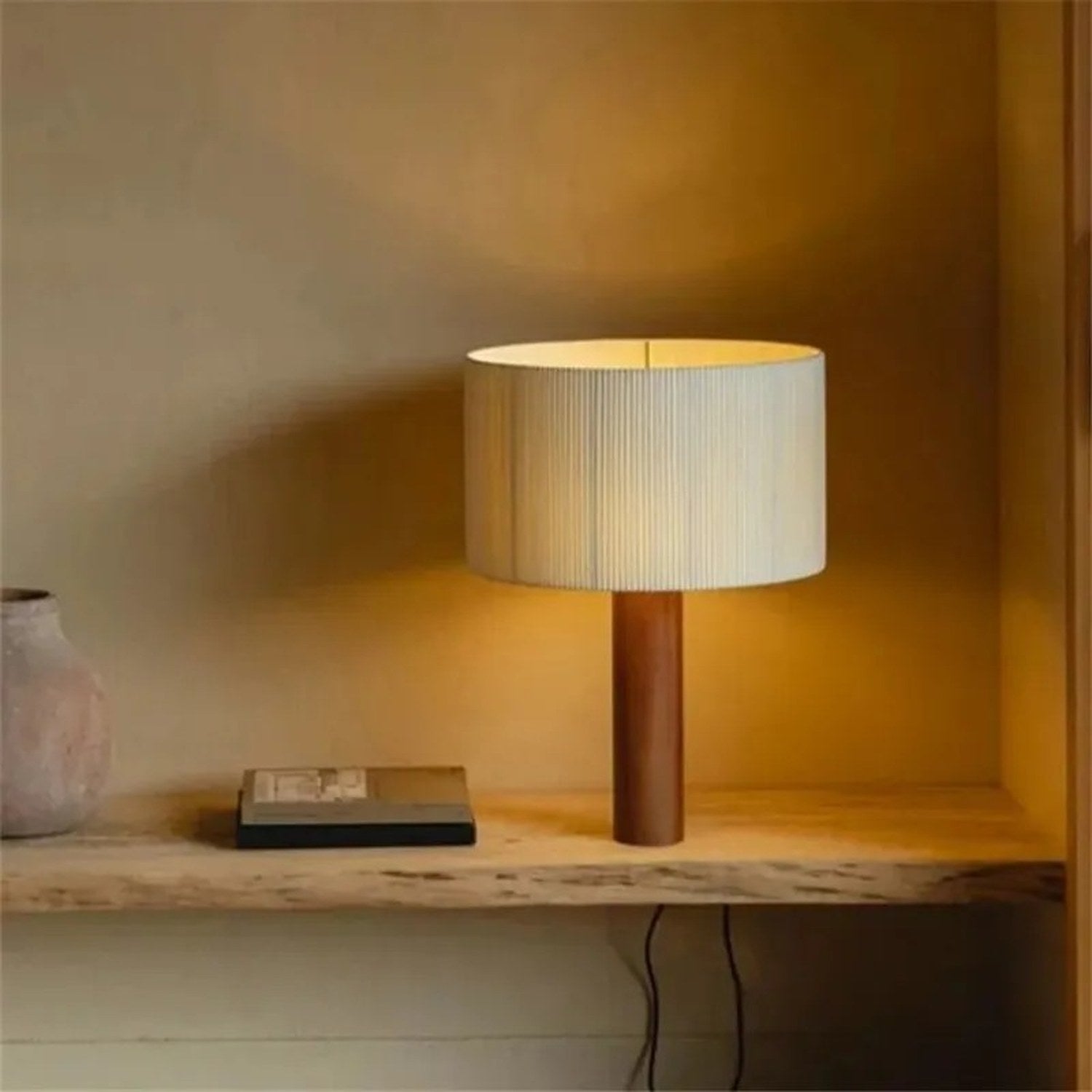 Lampe de table bois massif abat-jour plissé posée sur un meuble bas près d'un vase