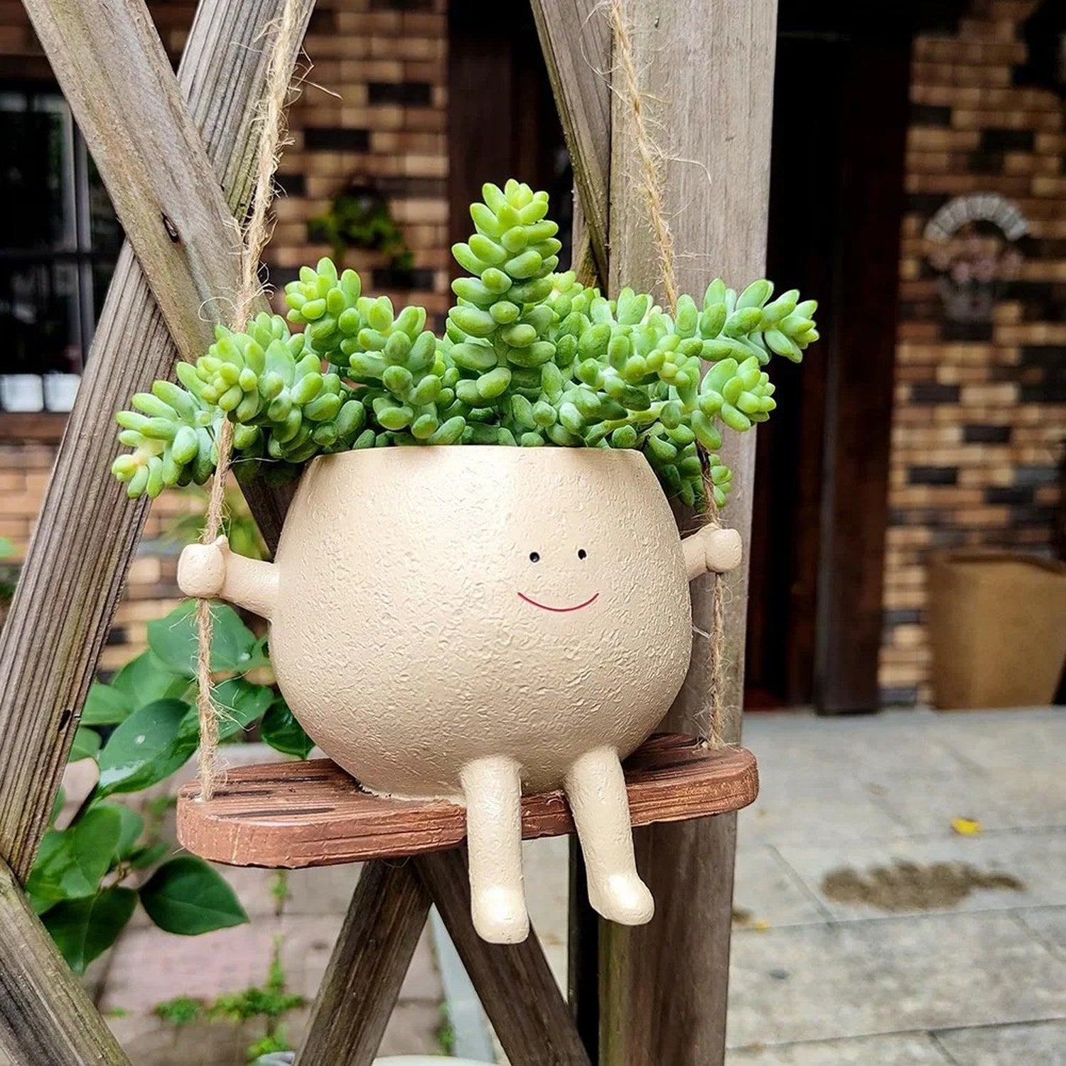 Pot de fleurs suspendu visage souriant avec succulente devant une maison en brique