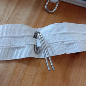 Galon fronceur blanc pour rideaux avec crochet métallique inséré sur une surface en bois