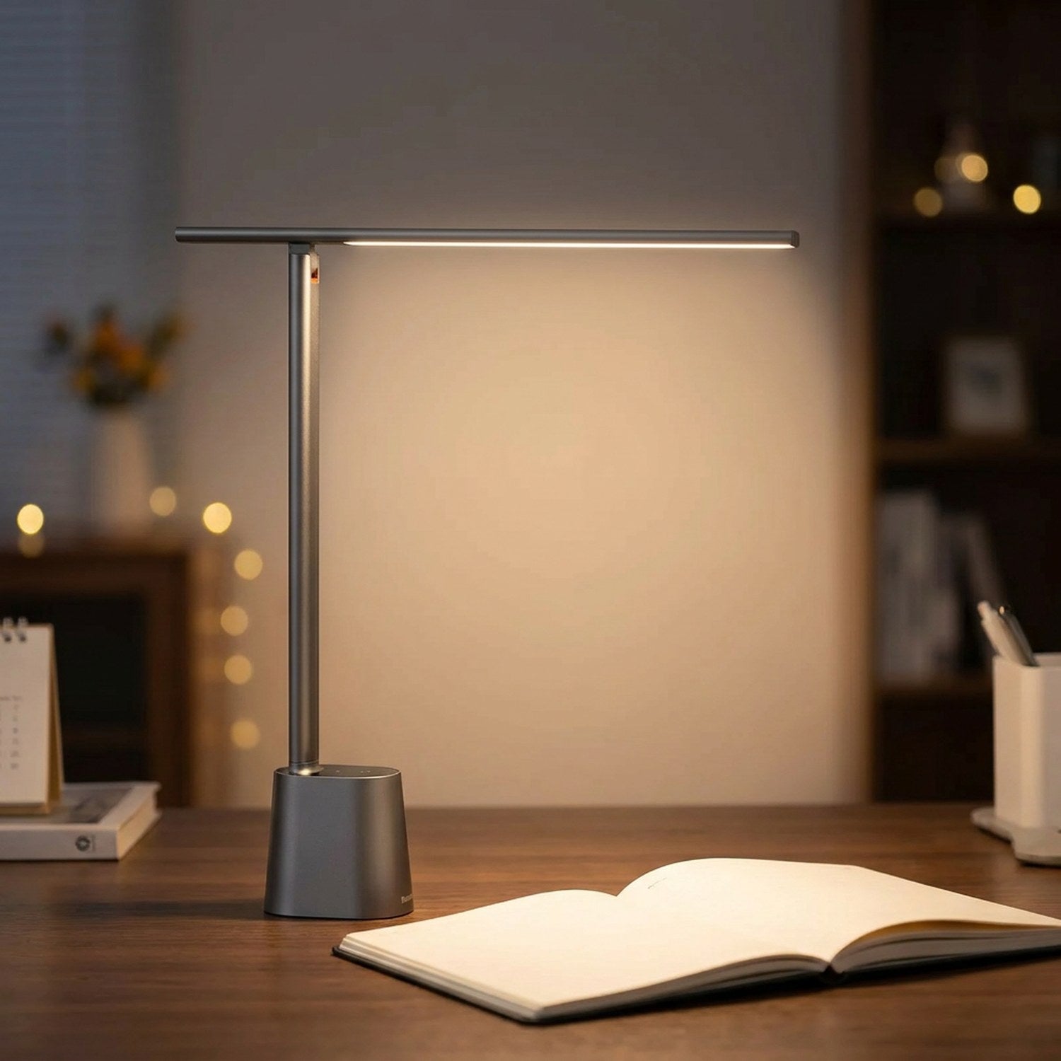 Lampe de bureau LED grise pliable allumée sur un bureau en bois foncé