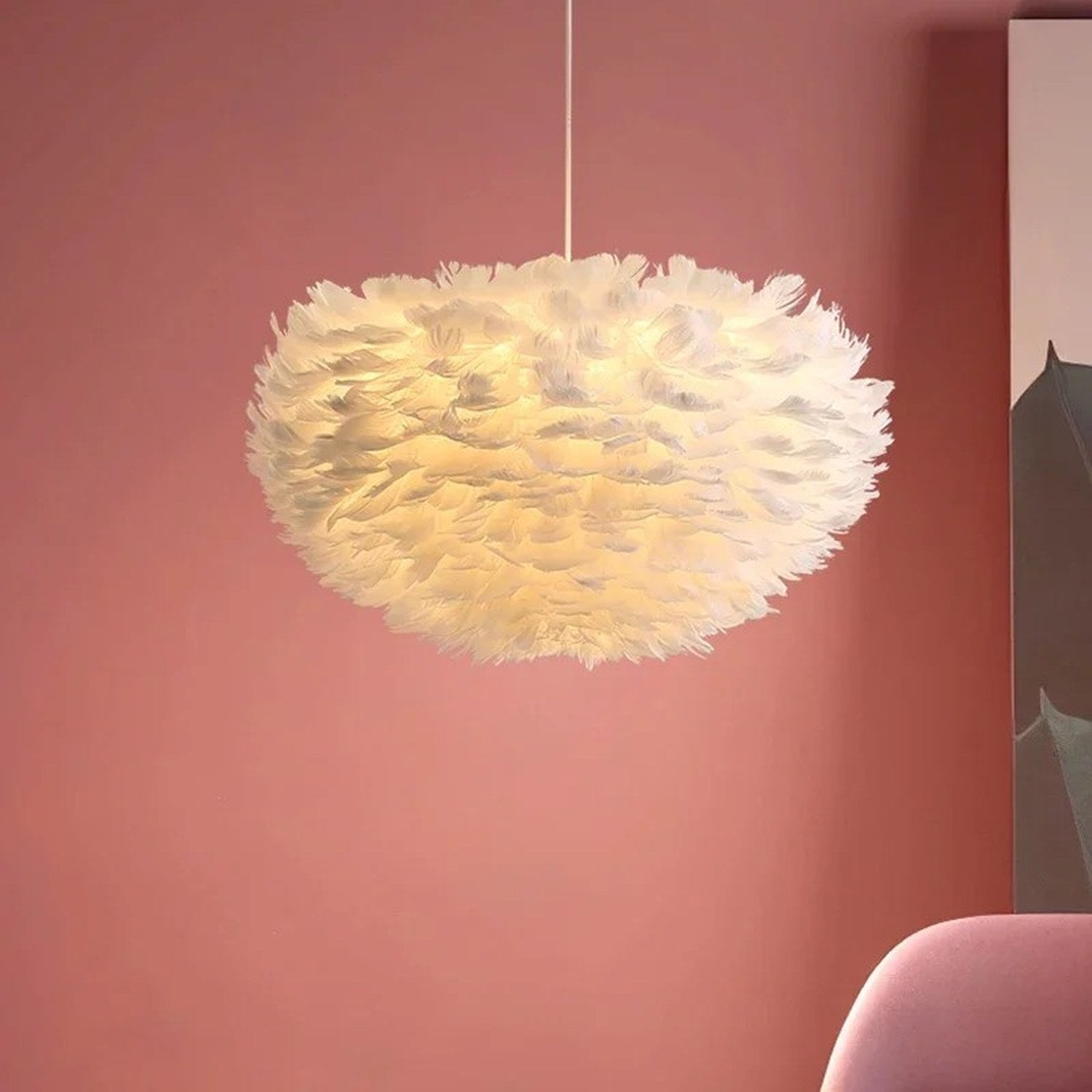 Suspension boule en plumes blanches allumée dans un salon aux tons roses