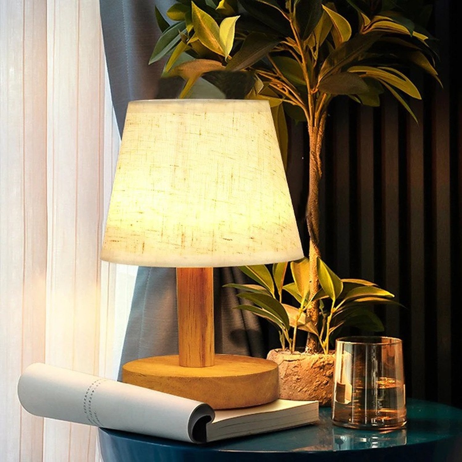 Lampe de chevet rétro allumée devant un rideau voilage avec une plante verte