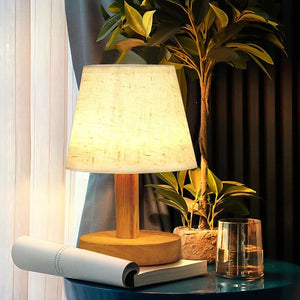 Lampe de chevet rétro allumée devant un rideau voilage avec une plante verte