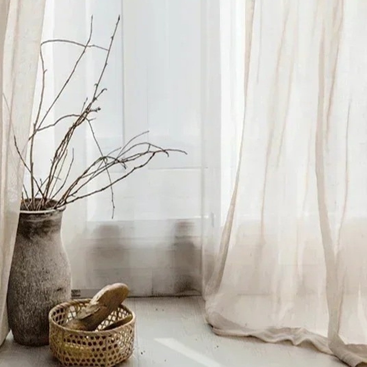 Détail du voilage tulle beige près d'une fenêtre avec vase en céramique et branches séchées