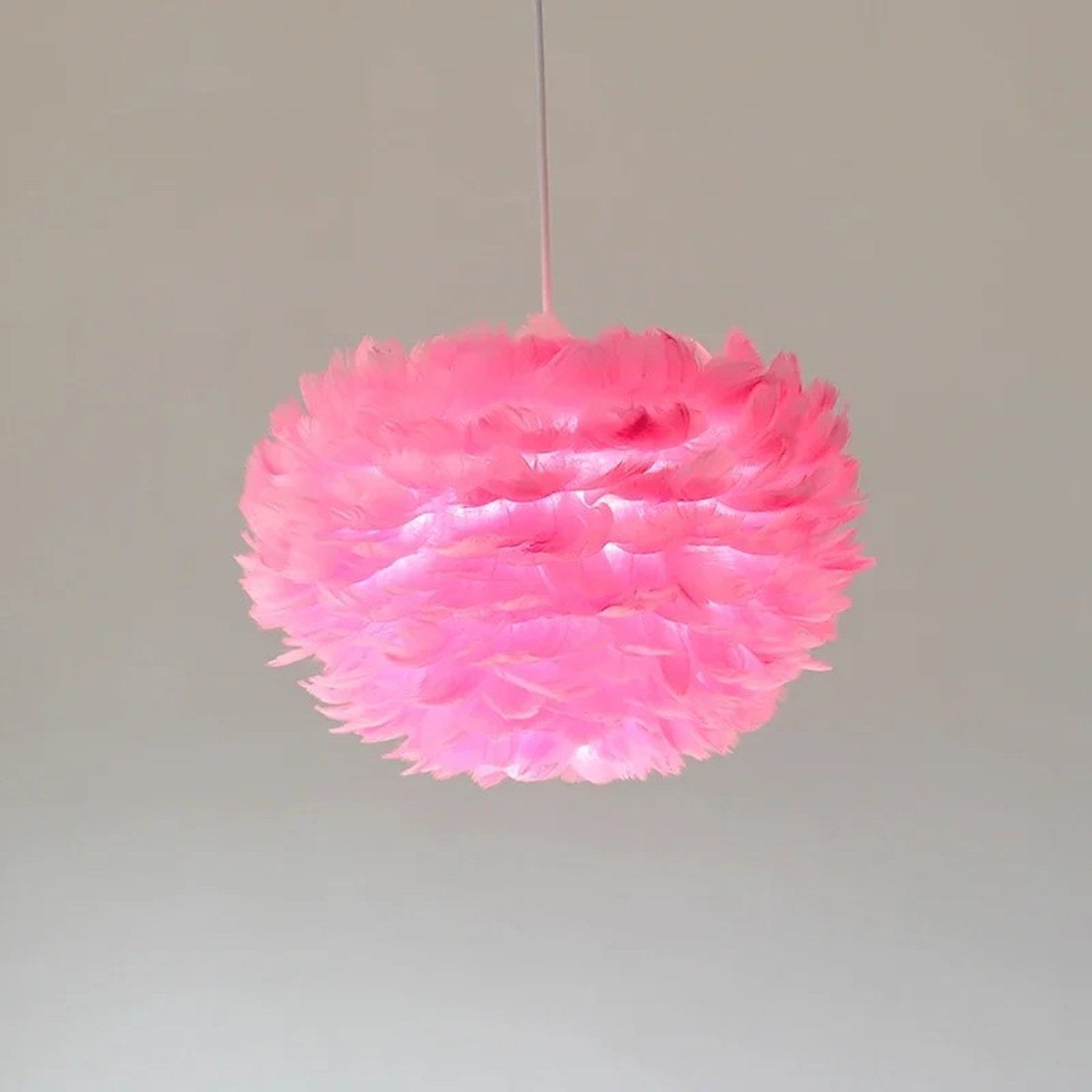Suspension boule en plumes roses allumée sur fond gris
