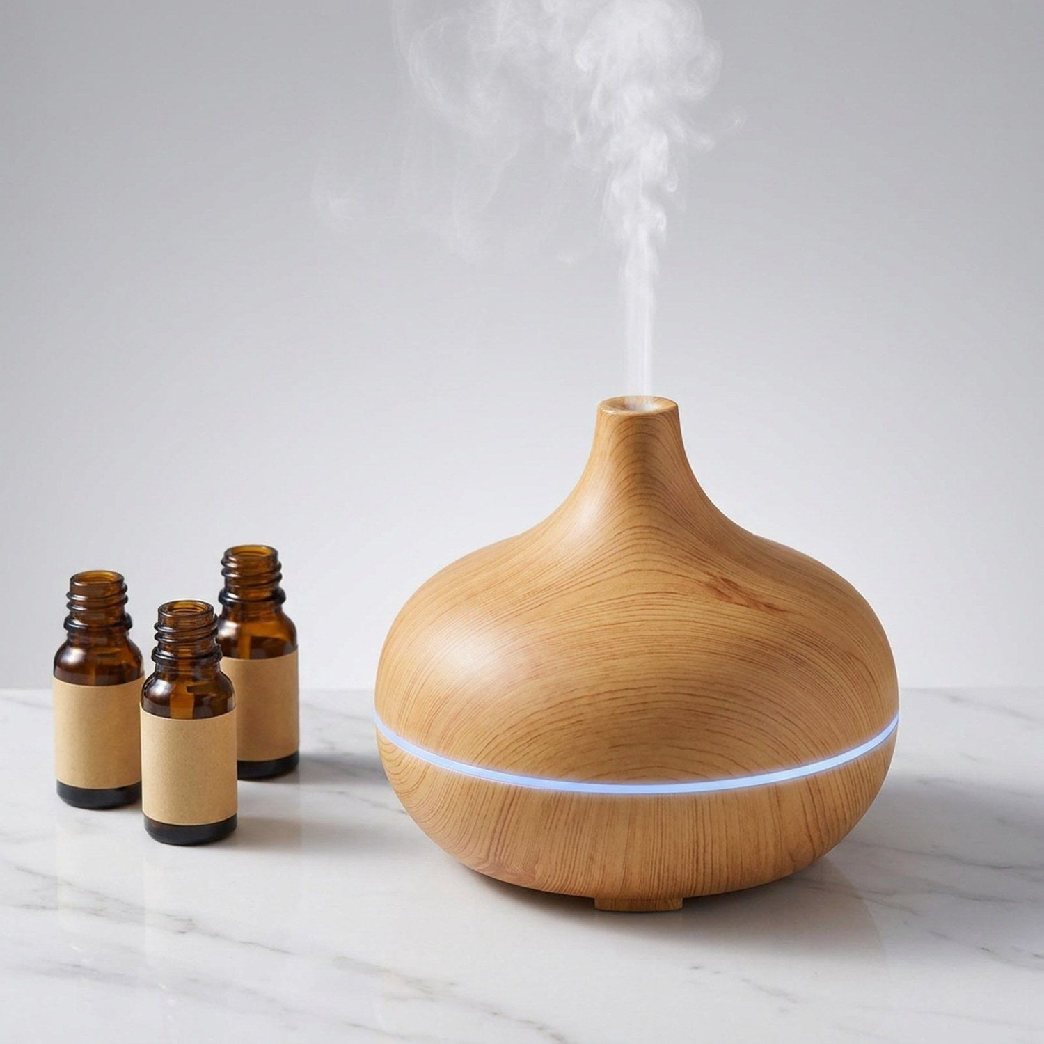 Diffuseur d'aromathérapie grain de bois clair sur marbre blanc avec flacons d'huiles essentielles ambrées, brume fine et lumière LED bleue