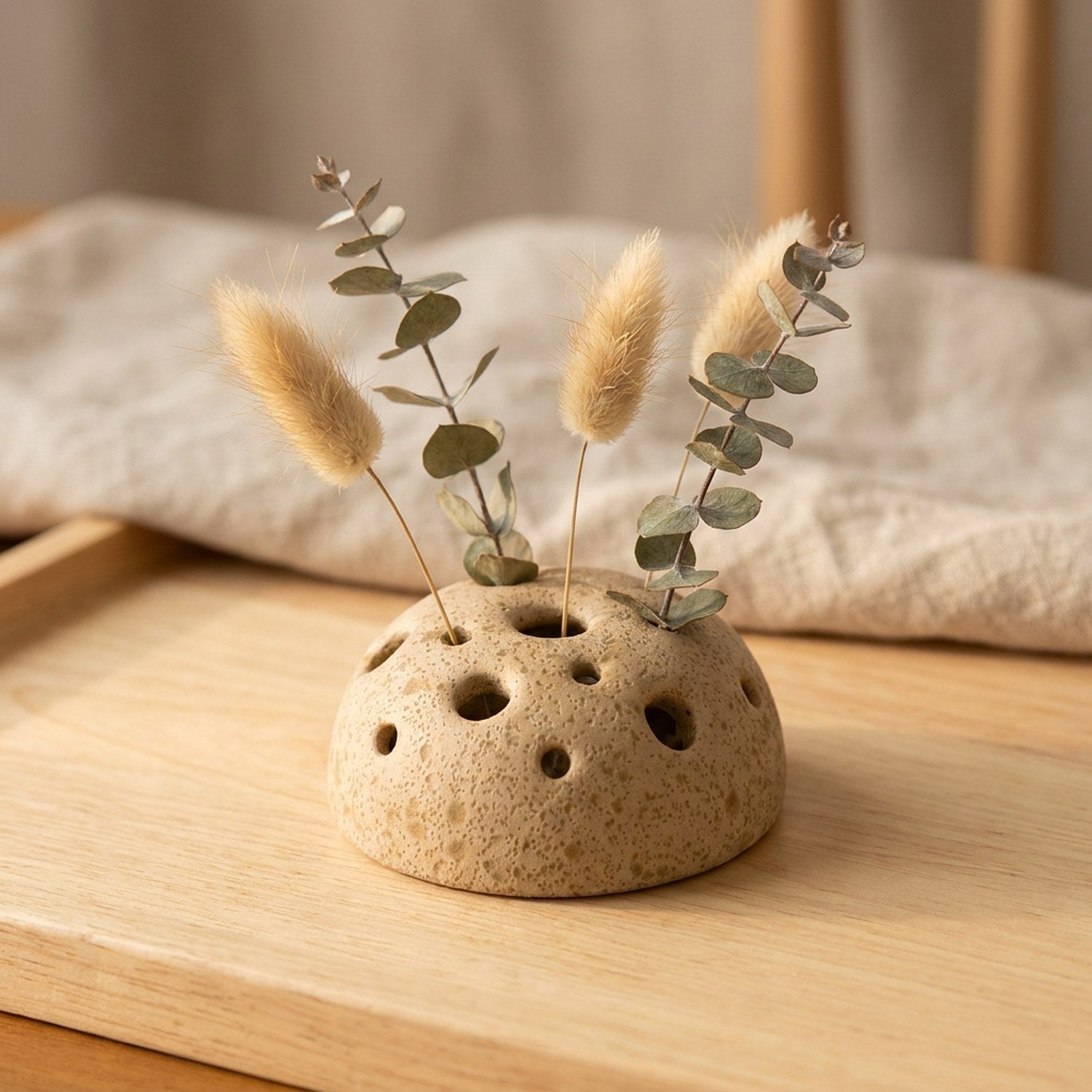 Vase en céramique beige en forme de graine de lotus avec fleurs séchées sur une table en bois