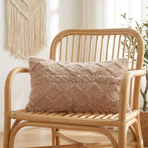 Housse de coussin lombaire en peluche beige à relief géométrique posée sur un fauteuil en bois