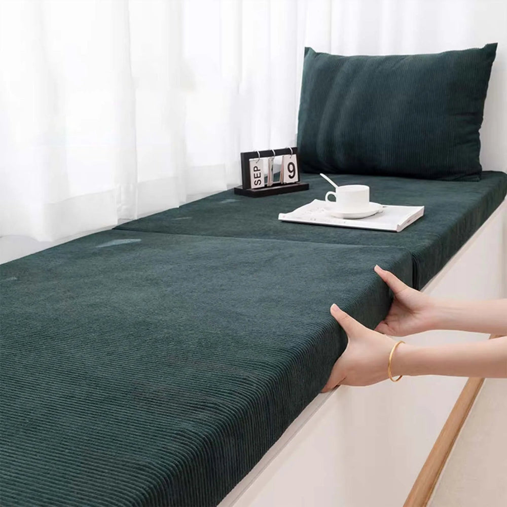 Coussin banquette en velours côtelé épais posé sur une assise près d’une fenêtre, avec texture côtelée visible et format rectangulaire épousant parfaitement la banquette.