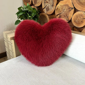Coussin canapé en forme de cœur au rendu duveteux et volumineux, posé sur un canapé texturé, avec une surface douce et épaisse qui invite à la détente.