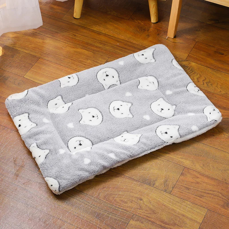 Un coussin chat confortable et chaleureux posé sur un sol en bois, avec une surface douce décorée de petits visages de chats, offrant un espace moelleux où un chat peut s’allonger pour se reposer.