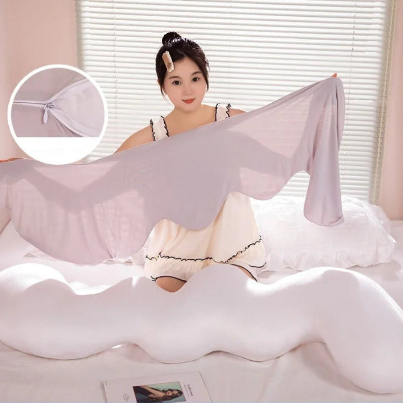 Un long coussin de lit ondulé blanc posé sur un lit, avec une forme sinueuse et moelleuse, tenu par une personne montrant sa souplesse et son aspect confortable.
