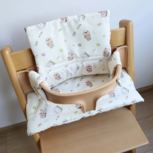 Un coussin de siège haute respirant à motif pour bébé installé sur une chaise haute en bois, avec des illustrations ludiques et une assise rembourrée couvrant le dossier et l’assise.