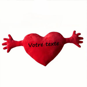 Un coussin personnalisé en forme de cœur avec un texte inscrit au centre, doté de bras stylisés, posé sur un fond clair pour mettre en valeur son design expressif.
