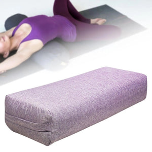 Un coussin yoga doux et confortable de forme allongée posé sur un tapis, utilisé pour soutenir le corps pendant des exercices de yoga et d’étirement.