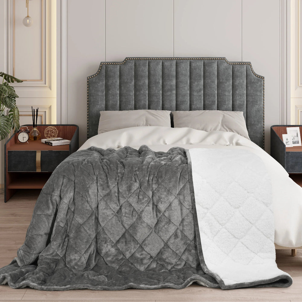 Une couverture lestée thérapeutique double face à texture matelassée, posée sur un lit élégant avec une tête de lit capitonnée, créant une ambiance chaleureuse et apaisante.