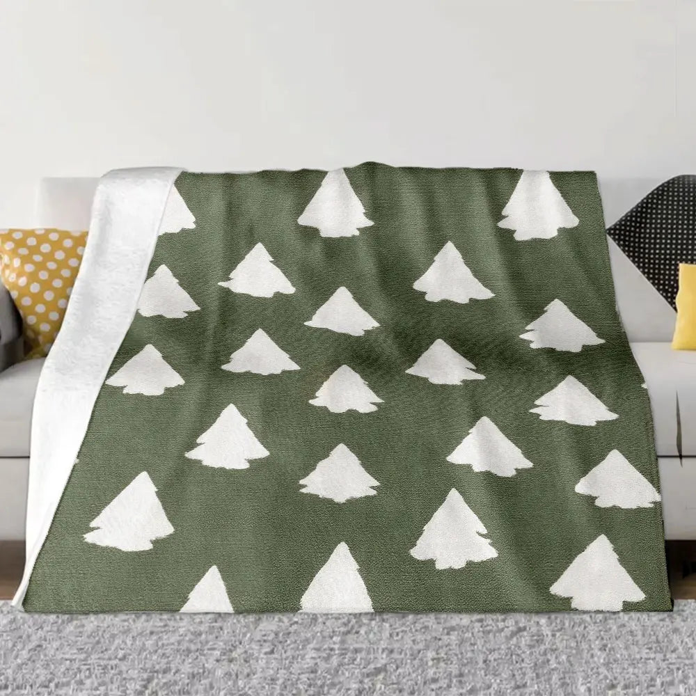 Un grand plaid à motifs sapins double-face étendu sur un canapé, avec des formes de sapins répétées et une texture douce, créant une ambiance chaleureuse et hivernale.