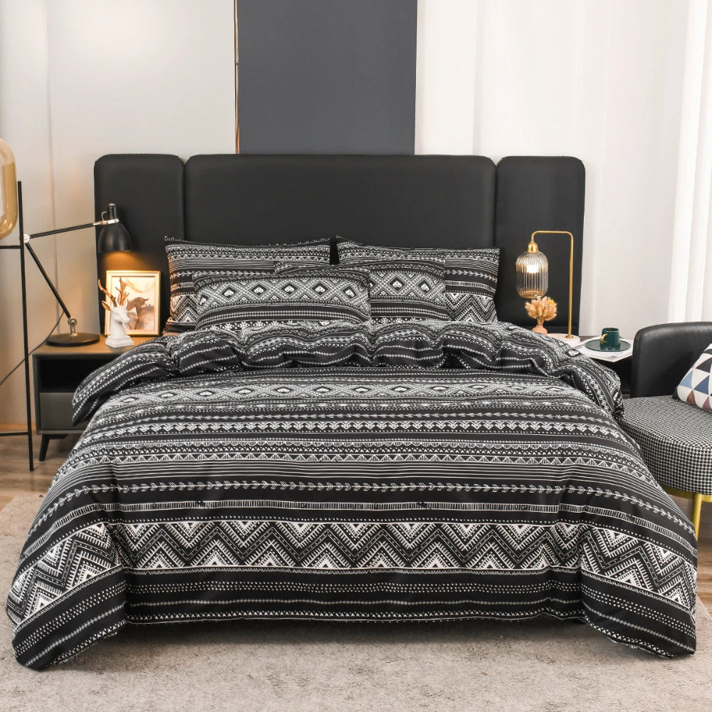 Parure de lit bohème motif Aztèque avec frises géométriques inspirées de l’art traditionnel, présentée sur un lit dans une chambre moderne avec tête de lit sombre et lampes décoratives.