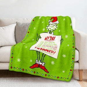 Un plaid Noël motif Grinch posé sur un canapé, représentant le célèbre personnage portant un bonnet de fête.
