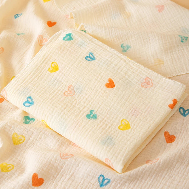 Un plaid bébé en gaze de coton gaufrée, délicatement plié, avec de petits motifs en forme de cœurs, posé sur un tissu assorti créant une ambiance douce et apaisante.
