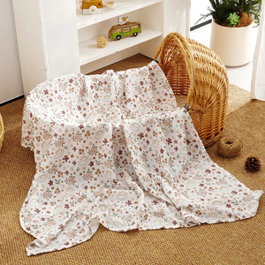 Un plaid bébé style bohème avec motifs floraux délicats, posé sur un berceau en rotin dans une chambre lumineuse à l’ambiance naturelle et chaleureuse.