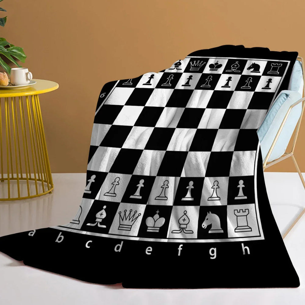 Un plaid cocooning motif échiquier noir et blanc drapé sur un fauteuil clair, avec un motif inspiré du plateau d’échecs et des pièces emblématiques visible sur toute la couverture.