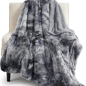 Un plaid en fausse fourrure gris ultra doux et épais, drapé sur un fauteuil clair, avec une texture moelleuse et un effet visuel chaleureux et cocooning.