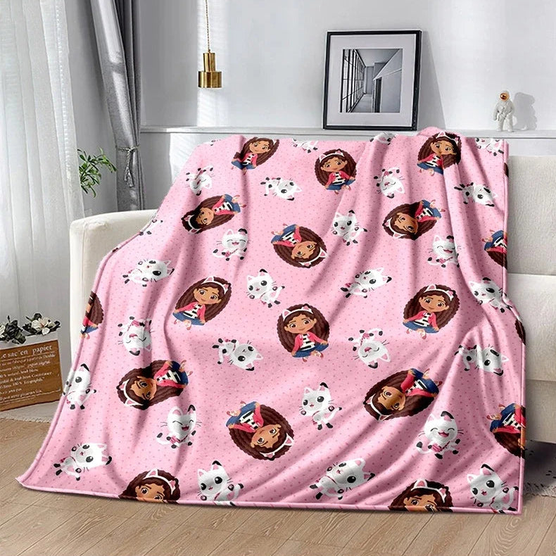 Un plaid enfant à imprimé Gabby Dollhouse recouvrant un canapé, avec des personnages ludiques répétés sur toute la surface, créant une ambiance douce et joyeuse dans un intérieur lumineux.