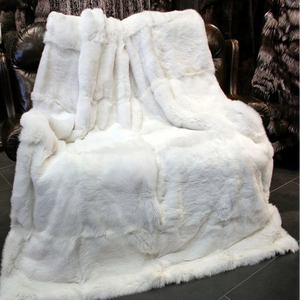 Un plaid fourrure de lapin blanc, épais et moelleux, drapé sur un fauteuil en cuir sombre, créant une ambiance chaleureuse et élégante dans un intérieur raffiné.