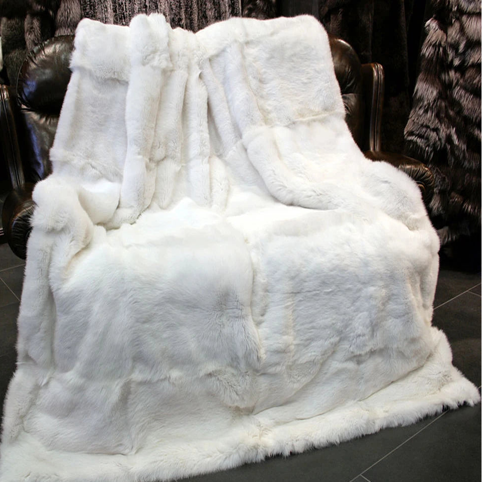 Un plaid fourrure de lapin blanc, épais et moelleux, drapé sur un fauteuil en cuir sombre, créant une ambiance chaleureuse et élégante dans un intérieur raffiné.