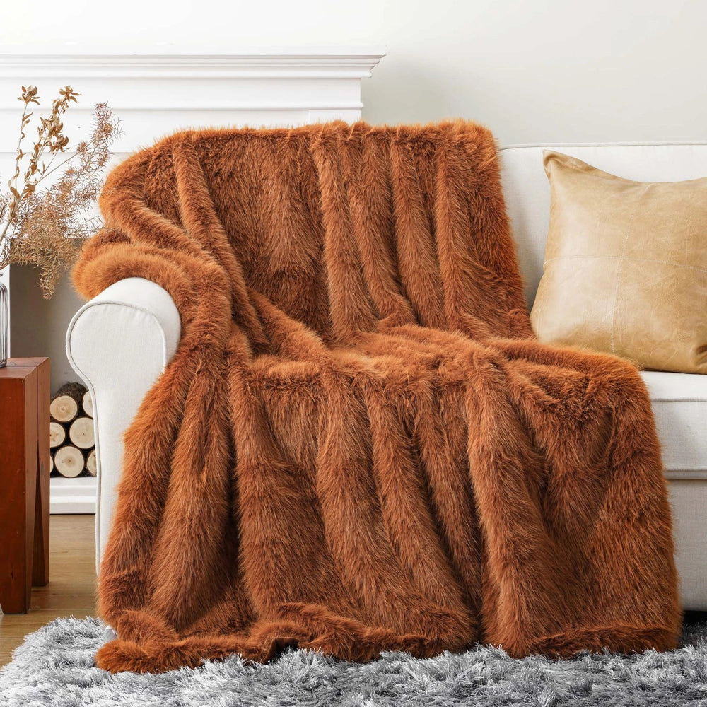 Un plaid fourrure épais et moelleux drapé sur l’accoudoir d’un canapé, avec une texture dense et duveteuse qui retombe en larges plis pour créer une ambiance chaleureuse et cocooning.