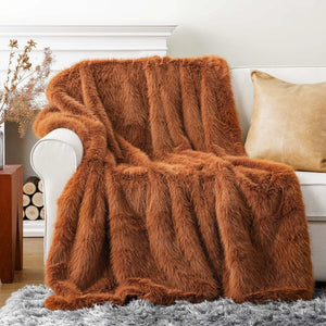 Un plaid fourrure épais et moelleux drapé sur l’accoudoir d’un canapé, avec une texture dense et duveteuse qui retombe en larges plis pour créer une ambiance chaleureuse et cocooning.