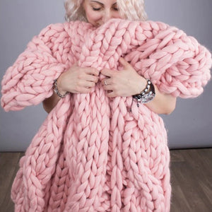 Une personne enveloppée dans un plaid grosse maille à relief rose, très épais et moelleux, mettant en valeur ses mailles volumineuses et son aspect cocooning.