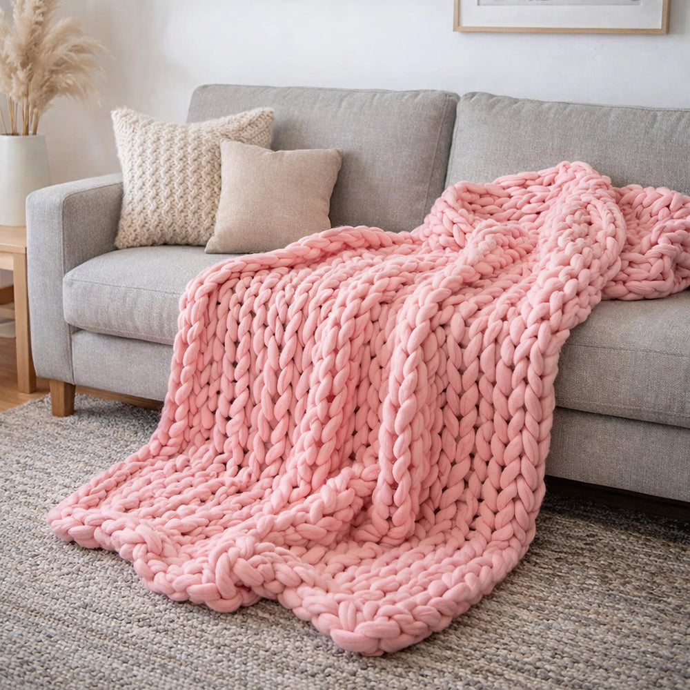 Un plaid grosse maille ultra-doux au tricot épais, délicatement posé sur un canapé, avec une texture généreuse et moelleuse qui invite à la détente.