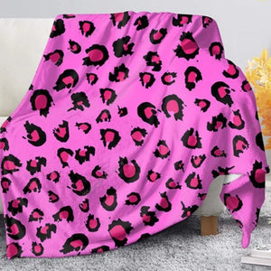 Un plaid léopard rose vif en flanelle douce, avec motifs noirs et roses, drapé sur un canapé dans un salon moderne avec coussins clairs.
