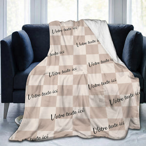 Un plaid personnalisé à carreaux avec texte est délicatement posé sur un canapé, mettant en valeur un motif quadrillé élégant avec plusieurs inscriptions personnalisées visibles sur le tissu.